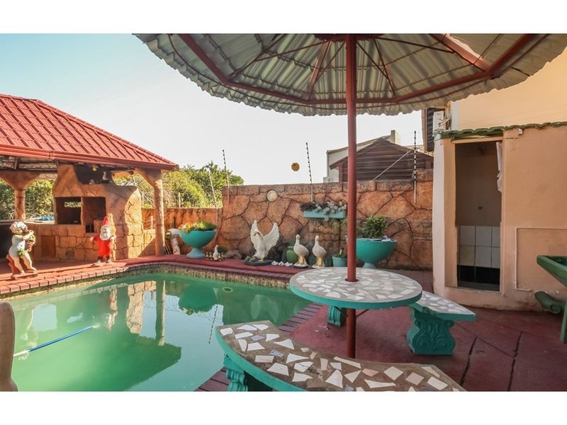 Outdoor pool area featuring a swimming pool, built-in braai, thatched lapa, and stone-clad boundary wall, providing a functional space for outdoor entertainment.