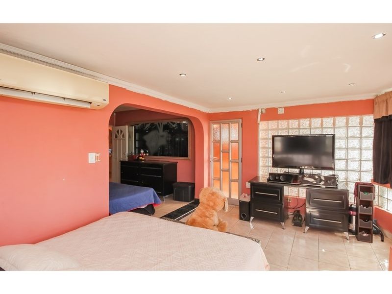 Spacious bedroom featuring tiled flooring, recessed downlighting, a unique glass block feature wall, and a wall-mounted split-system air conditioning unit.