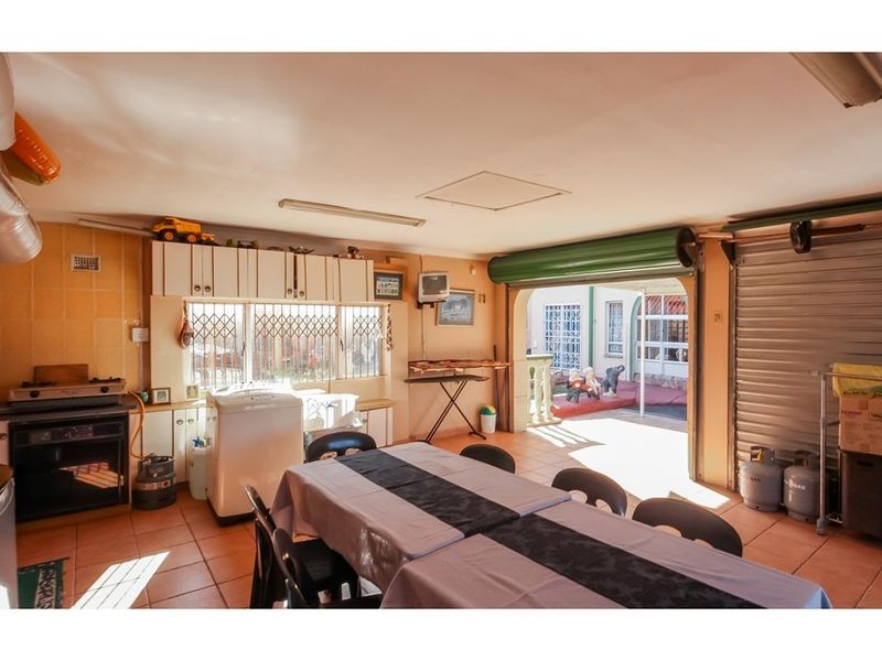 A multi-purpose utility space featuring tiled floors, built-in cabinetry, and a roller shutter door providing direct access to the outdoor patio area.