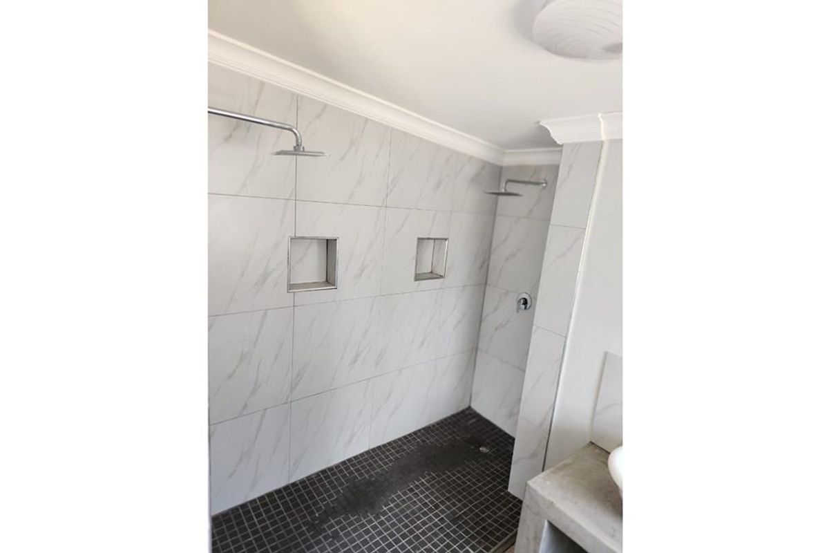 Modern walk-in shower featuring marble-look wall tiles, dark mosaic floor tiles, dual shower heads, and built-in recessed shelving niches.