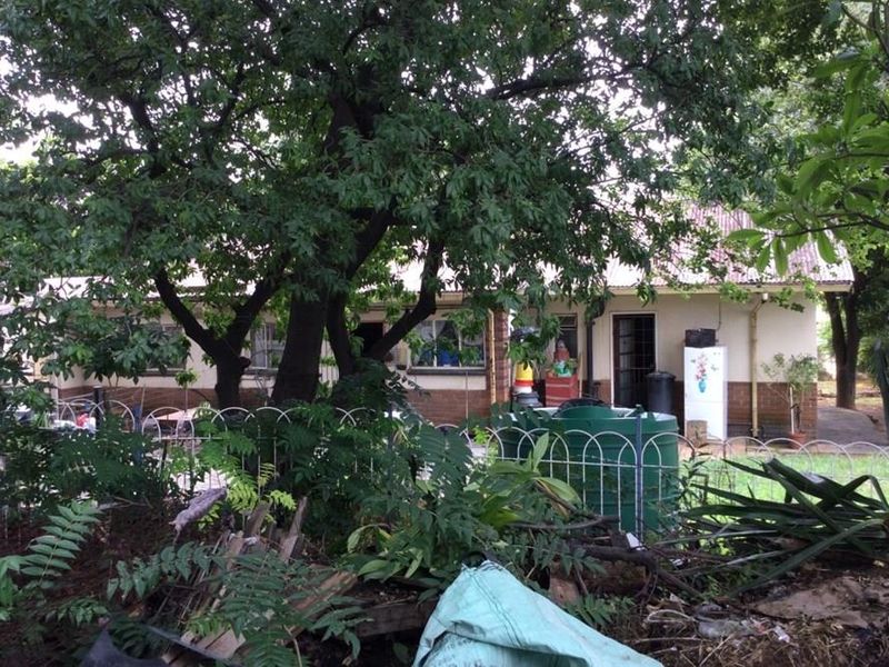 Rear view of the property featuring a garden area with mature trees, a metal fence, and access to the rear building elevation.