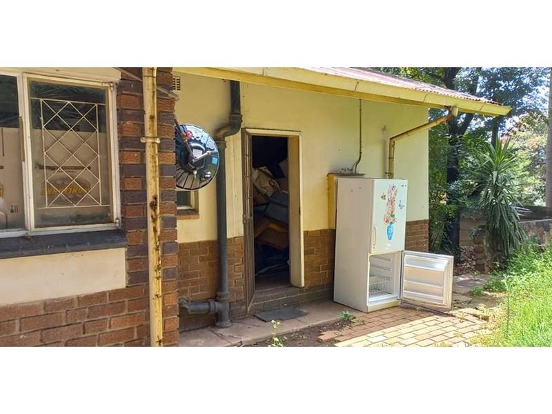 Exterior view of the rear of the house featuring brick facade, paved area, and access to a utility space.