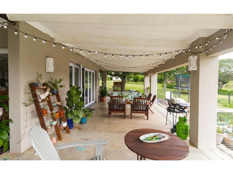 A spacious covered patio area featuring a concrete floor, structural pillars, and direct access to the garden, ideal for outdoor entertaining.
