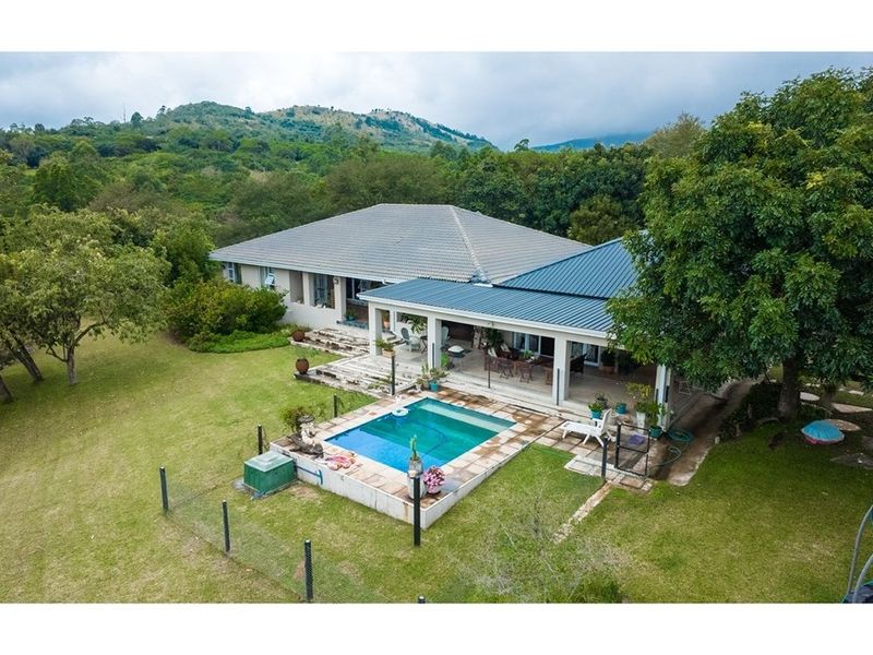 Aerial view of a small holding featuring a residential dwelling with a covered patio, swimming pool, and expansive surrounding garden with mountain views.