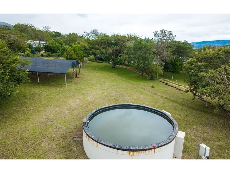 Aerial view of the small holding grounds featuring a large circular water storage tank and a shaded agricultural structure set within a landscaped garden.