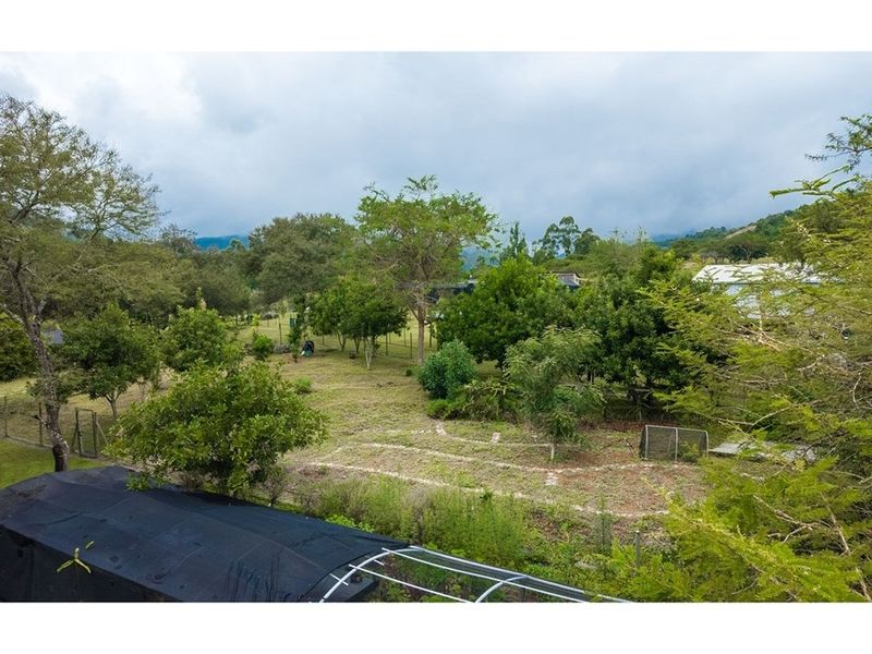 An elevated view of the property grounds featuring established trees, open garden space, and perimeter fencing on this small holding.