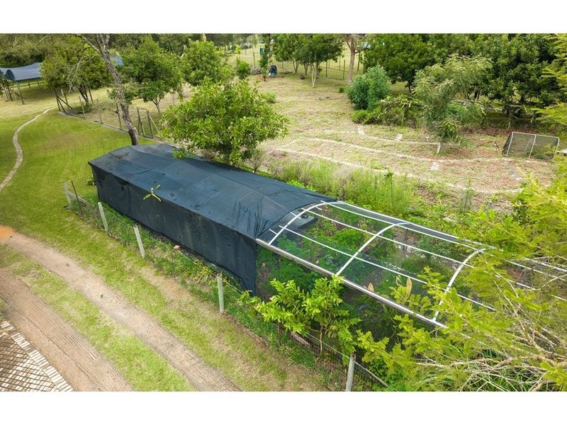 Aerial view of a small holding featuring a large tunnel-style greenhouse structure with shade netting and surrounding garden area.