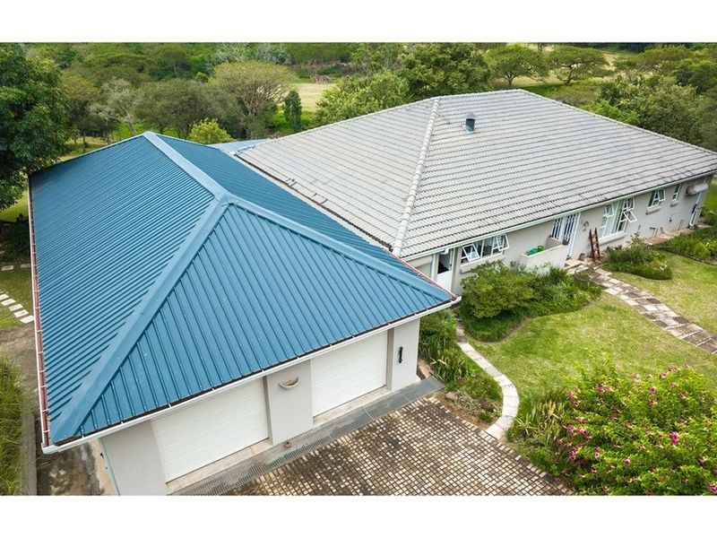 Aerial view of the property featuring a double garage with a blue metal roof and the main dwelling with a tiled roof and paved driveway.