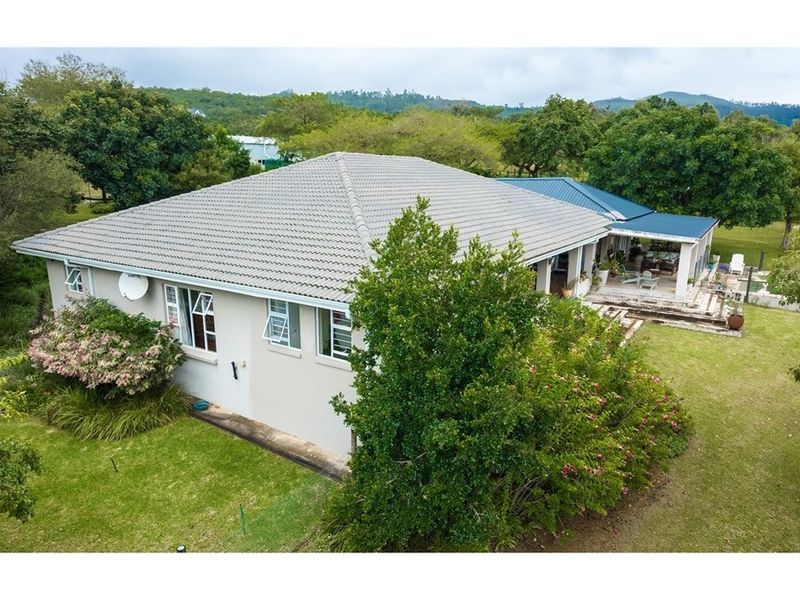 Aerial view of the property showing the main dwelling with a tiled roof, surrounding garden, and a covered patio area.