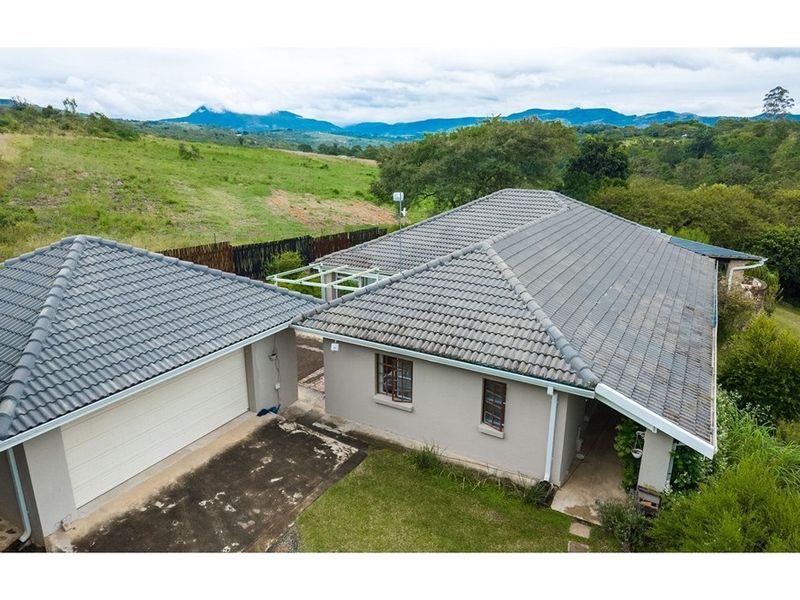 Aerial view of the property featuring a tiled roof dwelling, attached garage, and expansive surrounding landscape with mountain views.