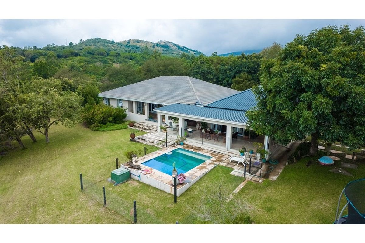Aerial view of a small holding featuring a residential dwelling with a covered patio, swimming pool, and expansive surrounding garden with mountain views.