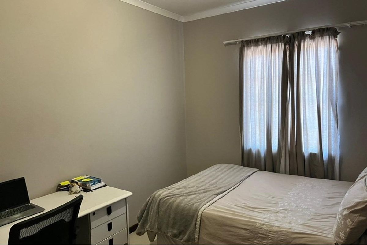 A functional bedroom featuring neutral wall tones, tiled flooring, and a window fitted with curtain rails.