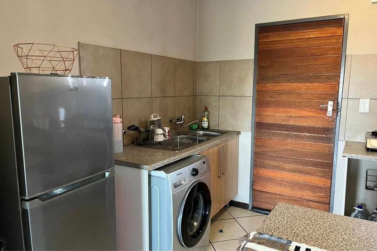 A functional kitchen area featuring tiled splashbacks, built-in cabinetry, a stainless steel sink, and dedicated space for laundry appliances.
