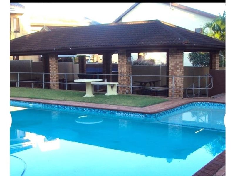 Outdoor pool area featuring a covered entertainment pavilion with brick pillars and a tiled roof, adjacent to a swimming pool with brick coping.
