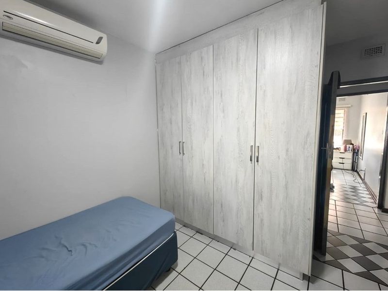 A bedroom featuring light-toned built-in wardrobes, tiled flooring, and a wall-mounted split-system air conditioning unit.