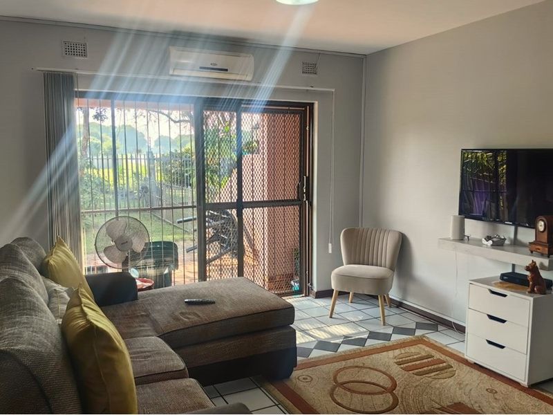 A comfortable living room featuring tiled flooring, a wall-mounted air conditioning unit, and a sliding glass door with a security gate leading outdoors.