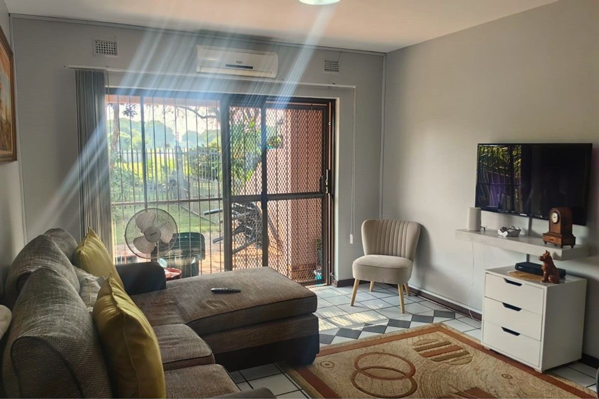 A comfortable living room featuring tiled flooring, a wall-mounted air conditioning unit, and a sliding glass door with a security gate leading outdoors.
