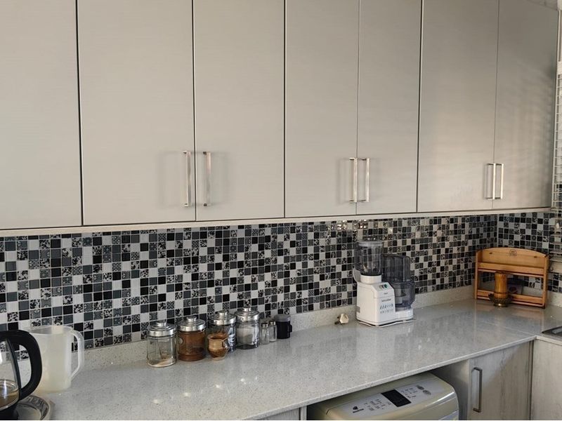 A modern kitchen featuring light-toned built-in cabinetry, a stone countertop, and a decorative mosaic tile backsplash.