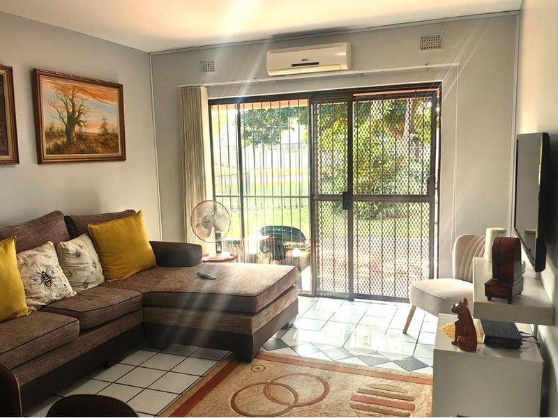 A living room featuring tiled flooring, a wall-mounted air conditioning unit, and a sliding glass door with a security gate leading outdoors.