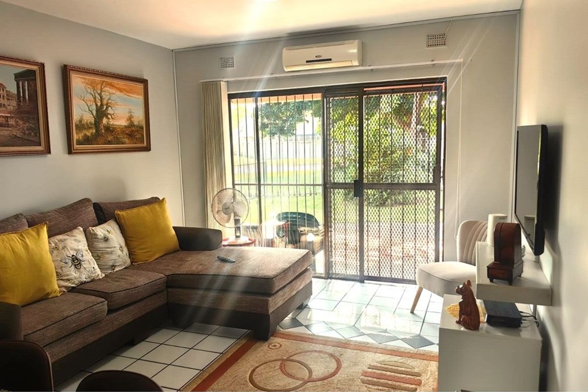 A living room featuring tiled flooring, a wall-mounted air conditioning unit, and a sliding glass door with a security gate leading outdoors.