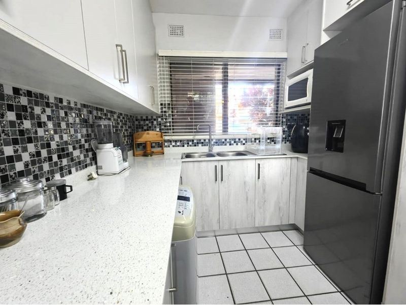 A functional kitchen featuring white cabinetry, stone countertops, a mosaic tile backsplash, and tiled flooring with a double basin sink.