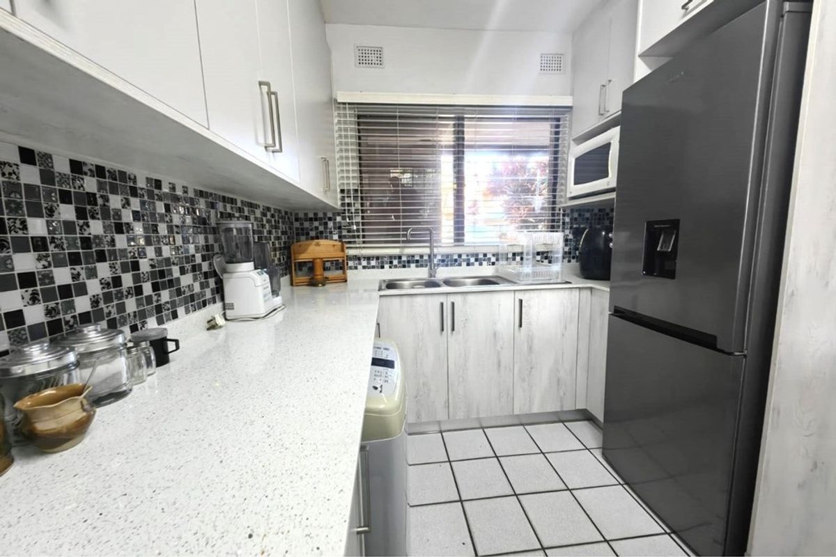 A functional kitchen featuring white cabinetry, stone countertops, a mosaic tile backsplash, and tiled flooring with a double basin sink.