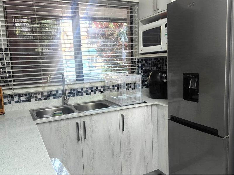 A functional kitchen featuring stone countertops, mosaic tile backsplash, double basin sink, and built-in microwave with light-toned laminate cabinetry.
