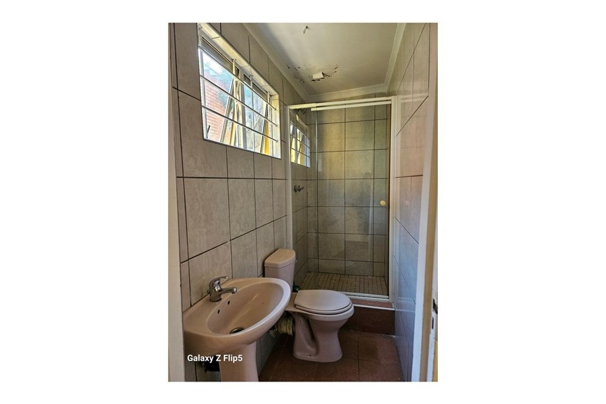 A compact bathroom featuring a shower enclosure, pedestal basin, and toilet, with visible ceiling damage and dated tiling throughout.