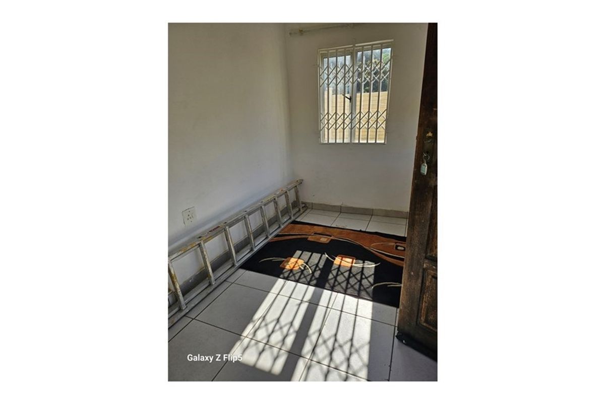 A small, empty room featuring tiled flooring and a window fitted with security bars.