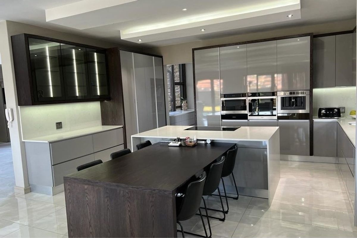 Modern open-plan kitchen featuring high-gloss cabinetry, integrated appliances, a large central island with a breakfast bar, and recessed ceiling lighting.