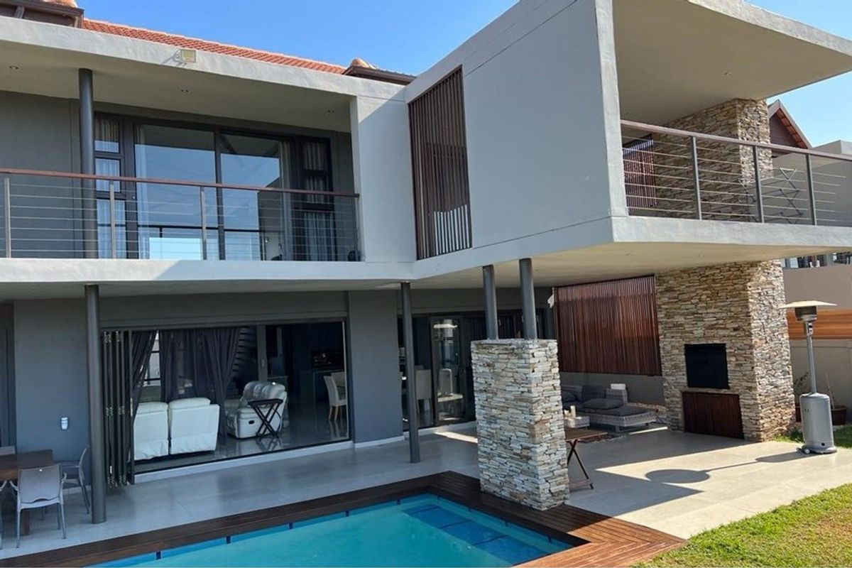 Modern double-story residence featuring a covered patio, built-in fireplace, swimming pool with timber decking, and upper-level balconies with stainless steel railings.