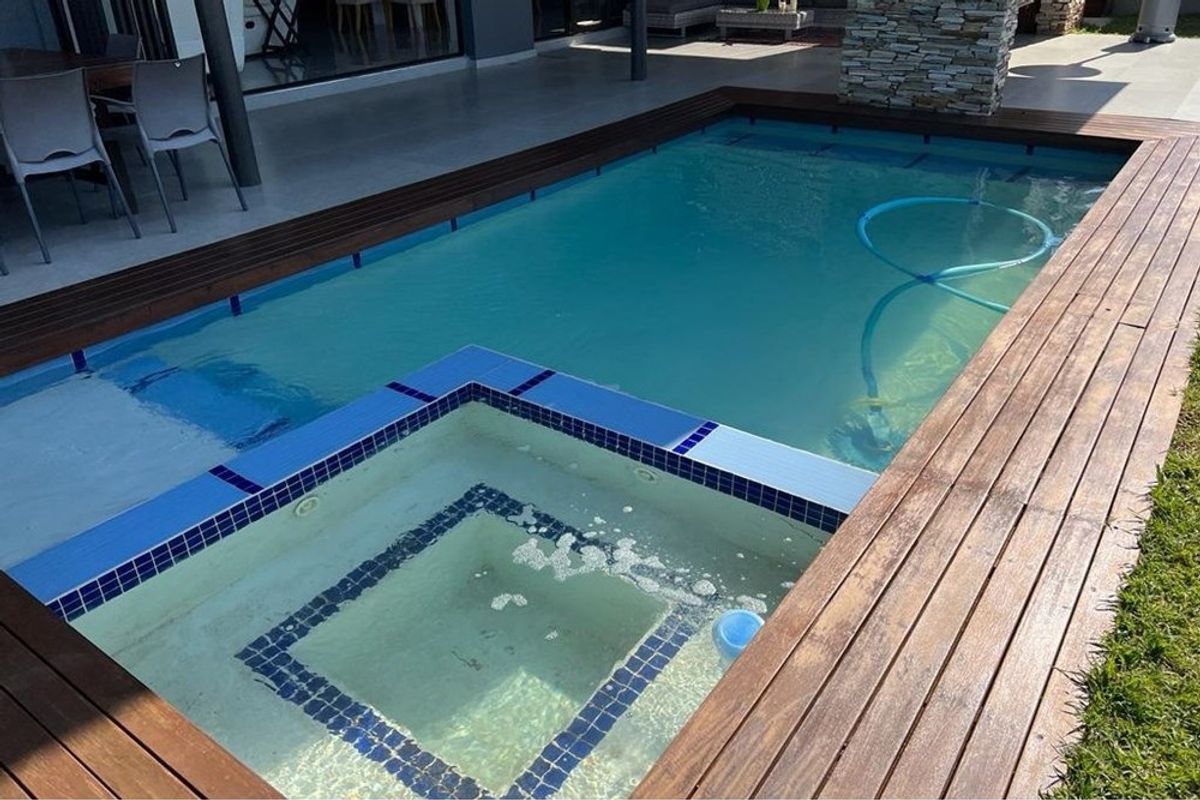 A well-maintained swimming pool featuring an integrated spa, surrounded by timber decking and adjacent to a covered patio area.