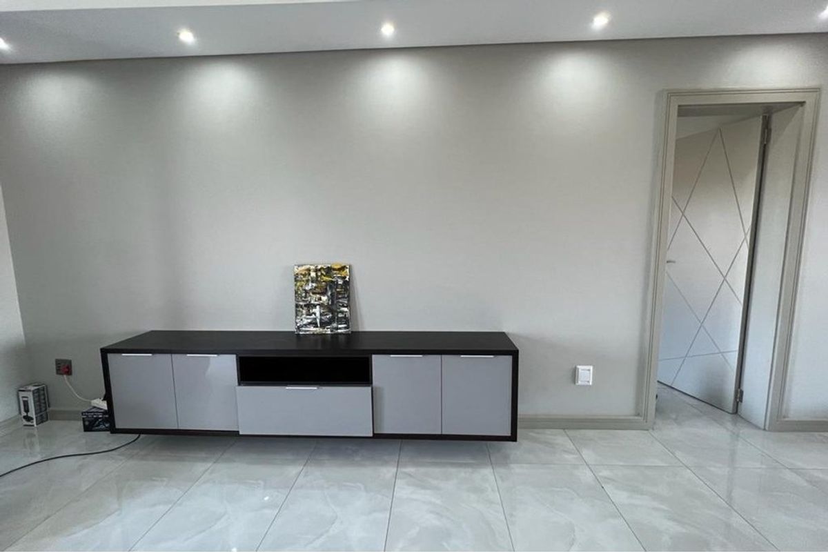 A modern living area featuring polished porcelain floor tiles, recessed ceiling downlights, and a contemporary interior door with geometric panel detailing.