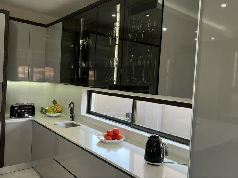 Modern kitchen featuring high-gloss cabinetry, stone countertops, integrated appliances, and sleek glass-fronted upper cabinets with under-cabinet lighting.