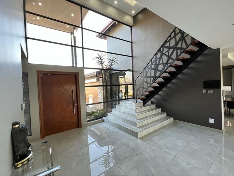 Spacious double-volume entrance hall featuring large floor-to-ceiling windows, modern tiled flooring, and a striking architectural staircase.