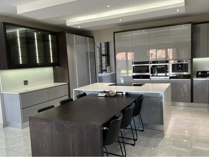 Modern kitchen featuring high-gloss cabinetry, stone countertops, a central island with integrated hob, and built-in appliances, complemented by sleek tiled flooring and recessed lighting.