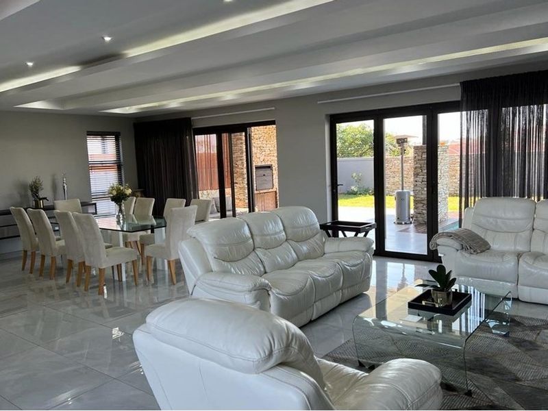 Spacious open-plan living and dining area featuring modern tiled floors, recessed ceiling lighting, and large glass doors opening to an outdoor patio.