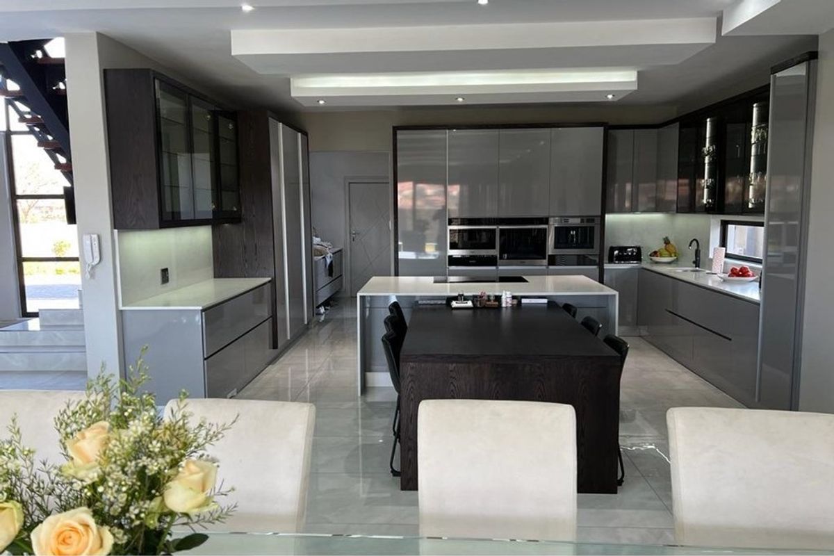 Modern, high-end kitchen featuring sleek grey cabinetry, a central island with stone countertops, built-in appliances, and polished tiled flooring.