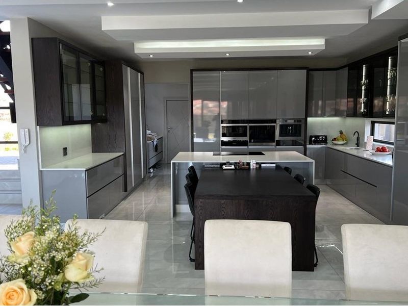 Modern, high-end kitchen featuring sleek grey cabinetry, a central island with stone countertops, built-in appliances, and polished tiled flooring.
