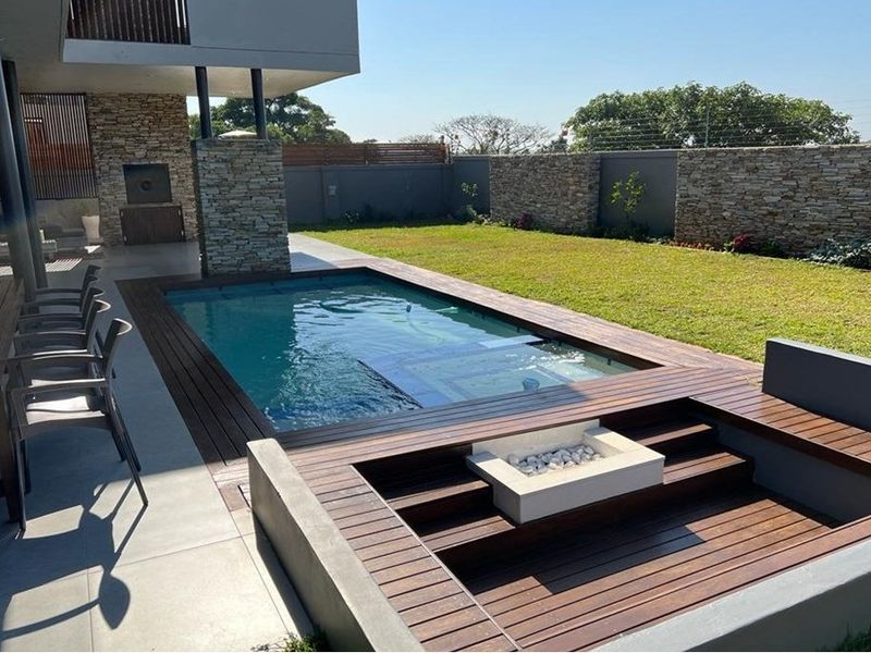 Modern outdoor entertainment area featuring a swimming pool, sunken fire pit, timber decking, and stone-clad boundary walls.
