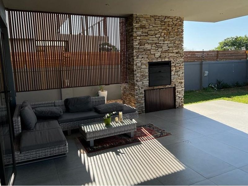 Covered patio featuring a built-in braai with stone cladding, timber privacy screening, and large format floor tiles, overlooking a private garden.