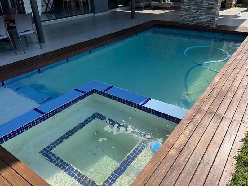 A well-maintained swimming pool featuring an integrated spa, surrounded by timber decking and adjacent to a covered patio area.