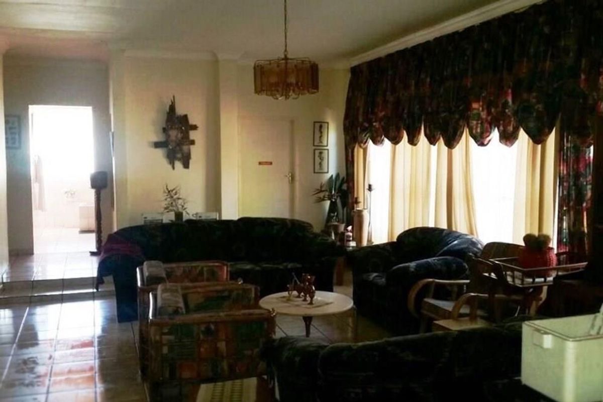 A spacious living room featuring tiled flooring, large windows with heavy drapery, and a central chandelier, providing a traditional and functional living space.