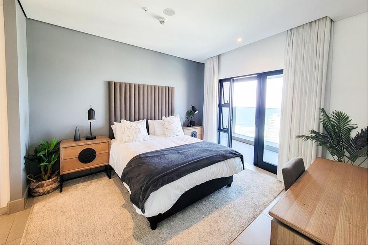 A modern, well-lit bedroom featuring a built-in headboard, tiled flooring, and direct access to a private balcony with expansive views.