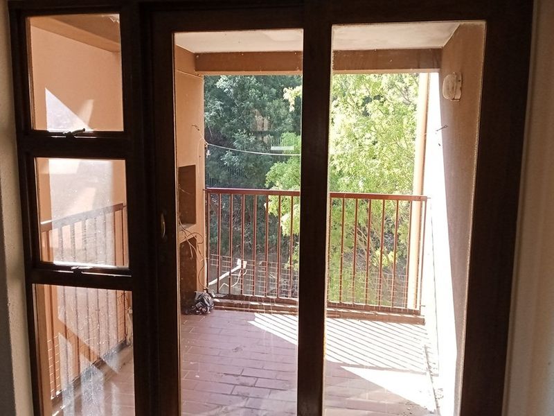 A covered balcony featuring tiled flooring and metal railings, accessible through a glass door, offering an outdoor space with a view of surrounding trees.