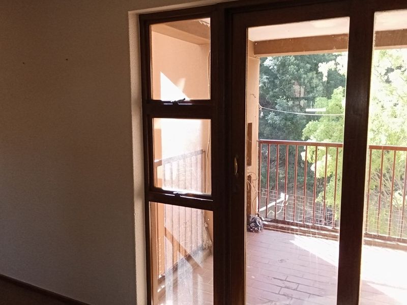 Interior view looking out through timber-framed glass doors onto a tiled balcony with metal railings.