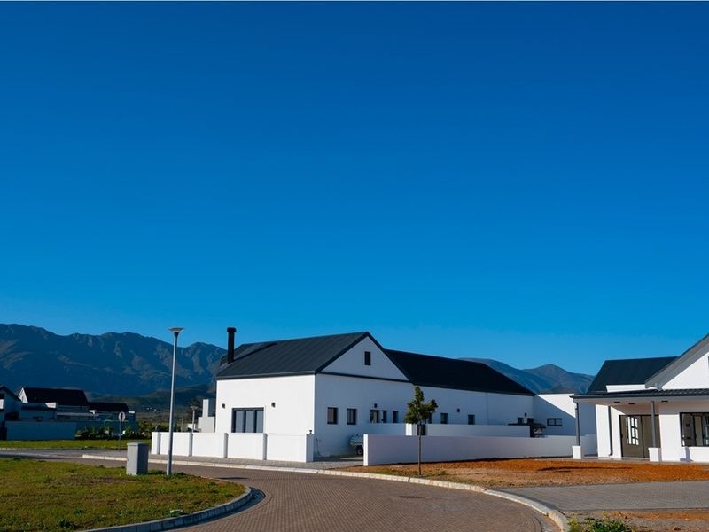 A modern residential property featuring white exterior walls, dark metal roofing, and a paved driveway, set against a scenic mountain backdrop.