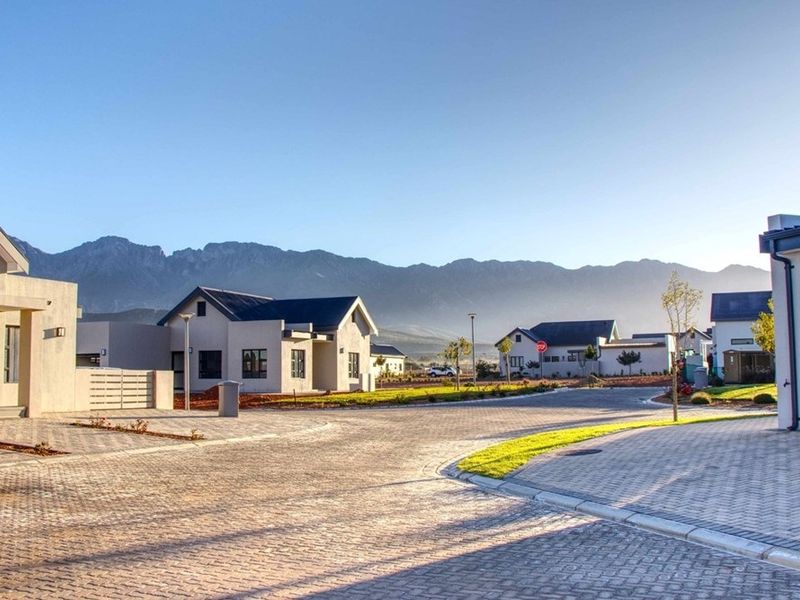 A clear street view of a modern residential estate featuring paved roads, well-maintained verges, and scenic mountain views in the background.