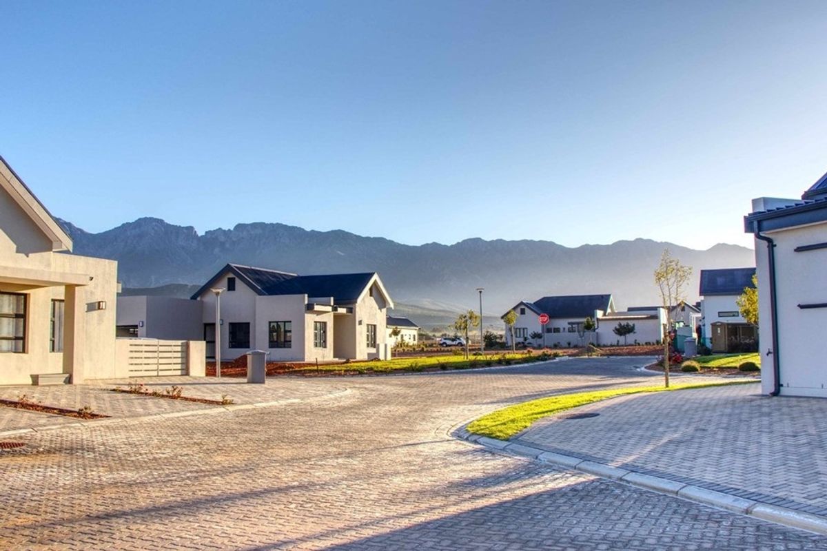 A clear street view of a modern residential estate featuring paved roads, well-maintained verges, and scenic mountain views in the background.