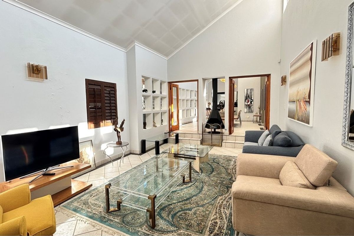 Spacious living room featuring high vaulted ceilings, tiled flooring, built-in display shelving, and a distinctive suspended fireplace connecting to adjacent living areas.